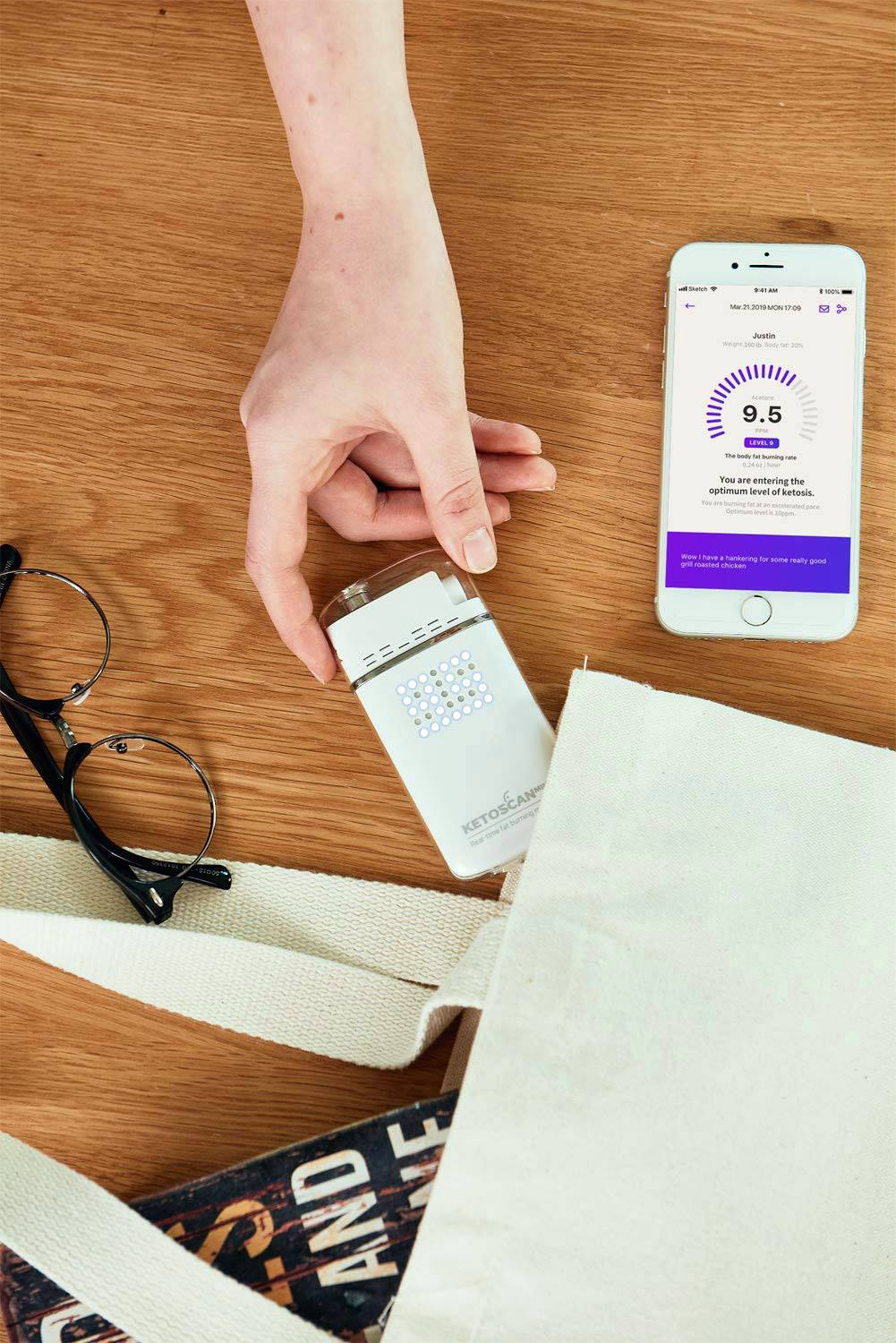 Eine Hand steckt ein tragbares Gerät in eine Tasche. Nebenbei liegt ein Smartphone mit einer offenen App, die '9.5' anzeigt.