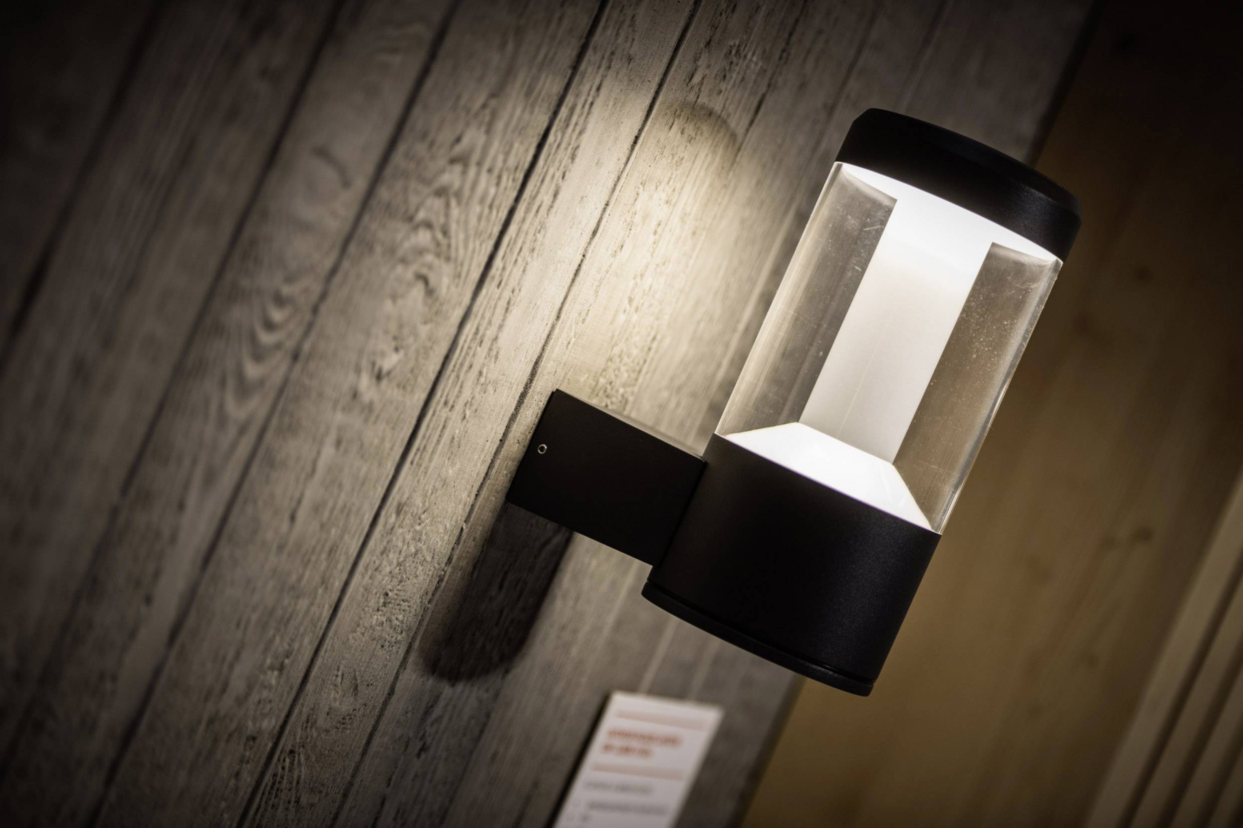 Außenwandleuchte mit modernem Design an einer Holzfassade montiert; Lichtstrahl beleuchtet die Wand.