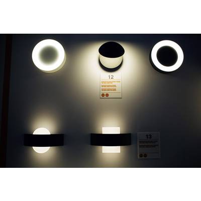 Verschiedene moderne Wandleuchten in hellem und dunklem Design auf grauer Wand ausgestellt. Zahlen 12 und 13 neben Leuchten.