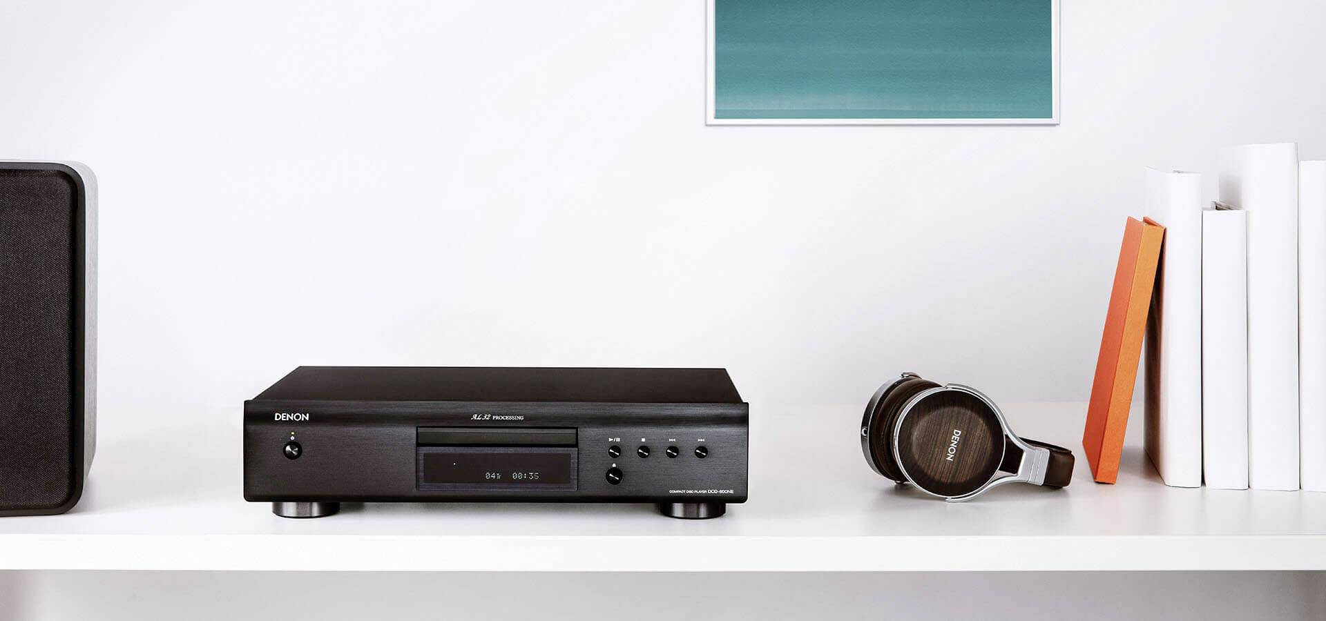 Auf einem weißen Regal stehen ein schwarz glänzender CD-Player, ein Kopfhörer, Bücher mit weißen Einbänden und ein Gemälde an der Wand.