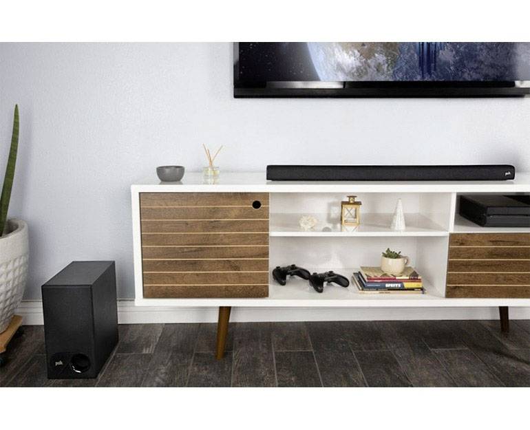 Weiße TV-Kommode mit Holzschubladen, darauf steht eine Soundbar. Daneben befinden sich Bücher, zwei Controller und Dekorationen.