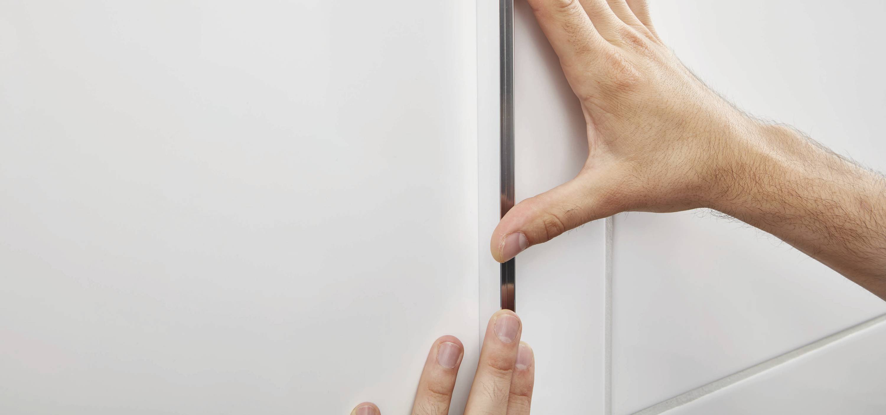 Zwei Hände überprüfen den Spalt zwischen zwei weißen Schranktüren, um die Ausrichtung und den Abstand zu kontrollieren.