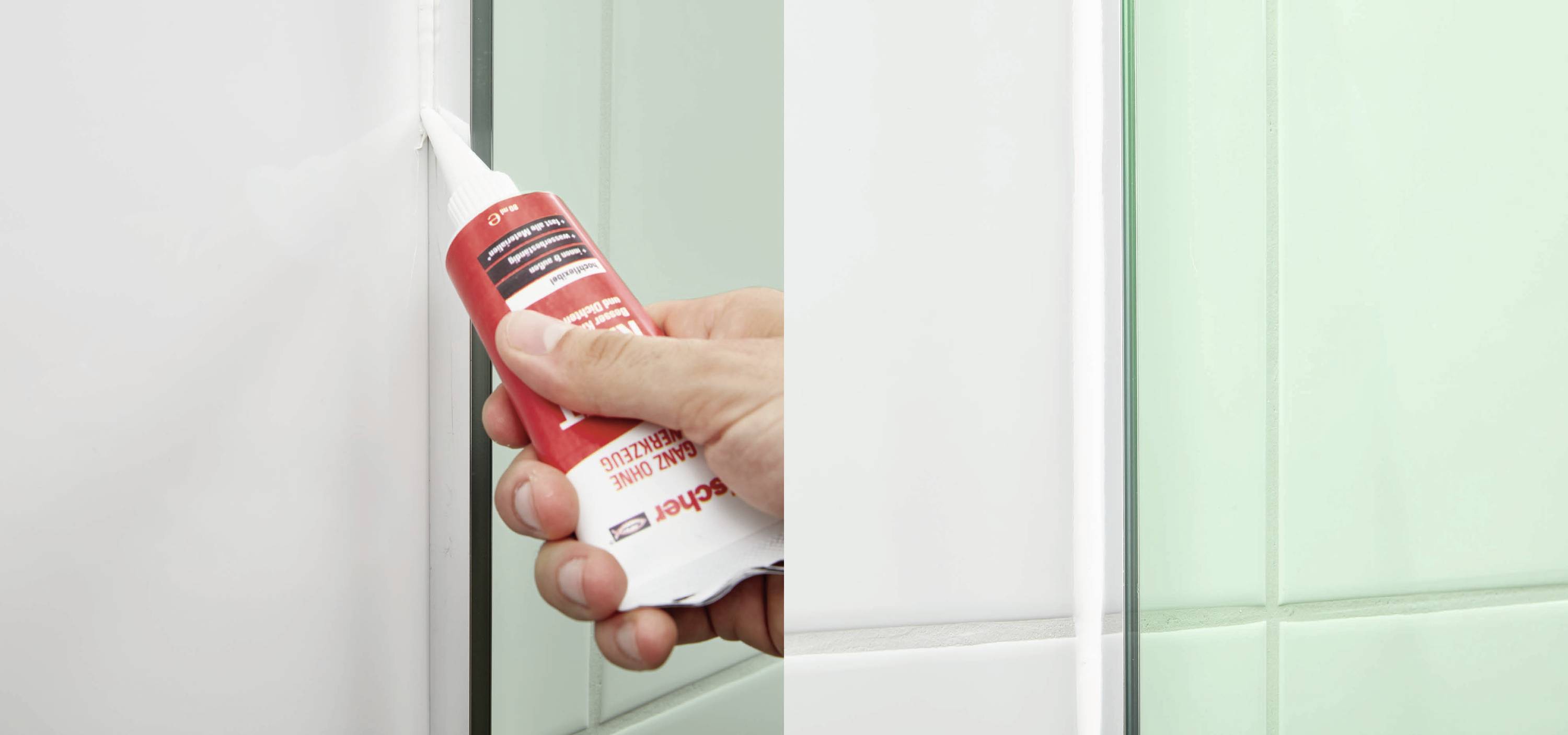 Eine Hand trägt mit einer Tube weißen Dichtstoff in eine Fuge zwischen hellen Fliesen auf, möglicherweise in einem Badezimmer.