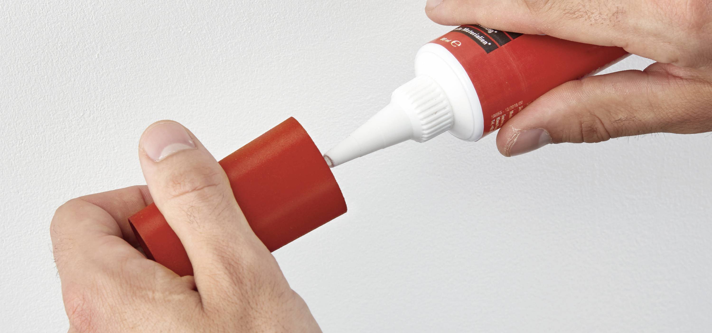 Zwei Hände öffnen eine rote Tube mit Dichtungskleber.