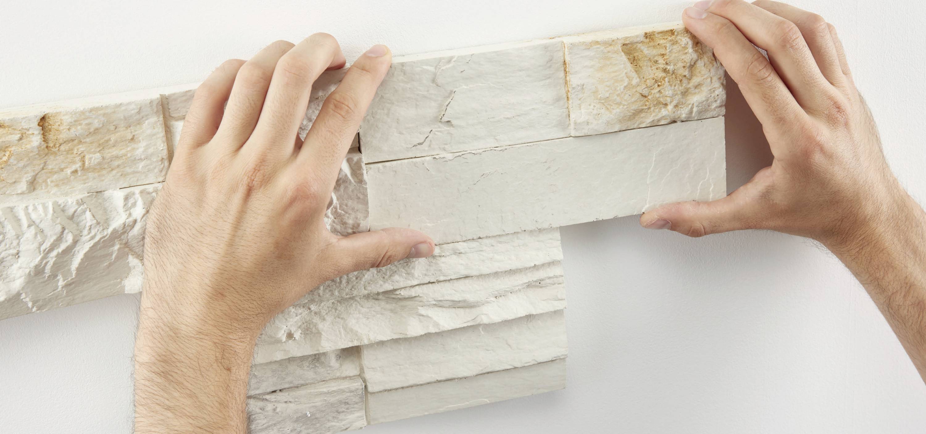 Eine Person befestigt weiße Steinverblender an einer Wand.