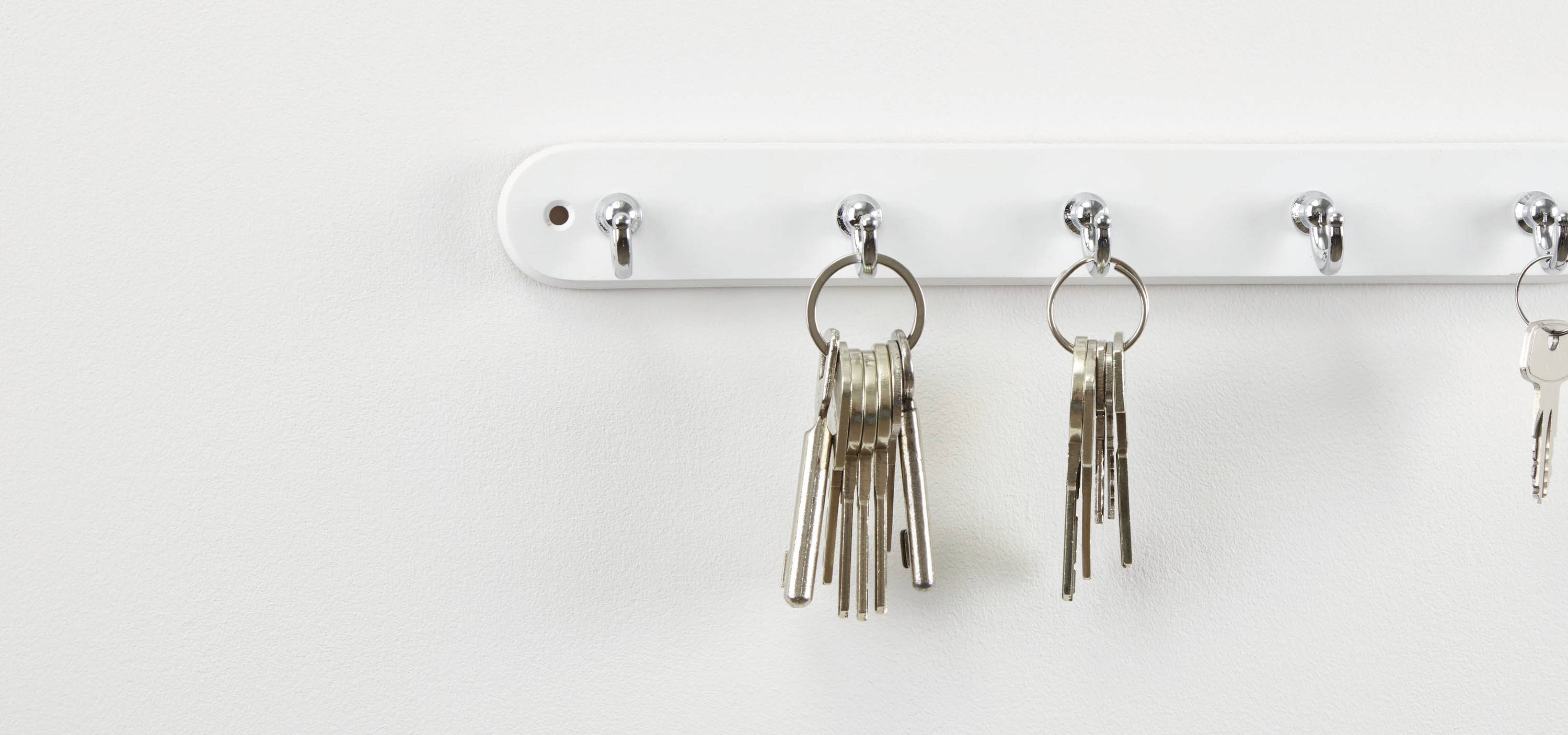 Mehrere Schlüssel hängen an einem weißen Schlüsselbrett mit Haken an einer weißen Wand.