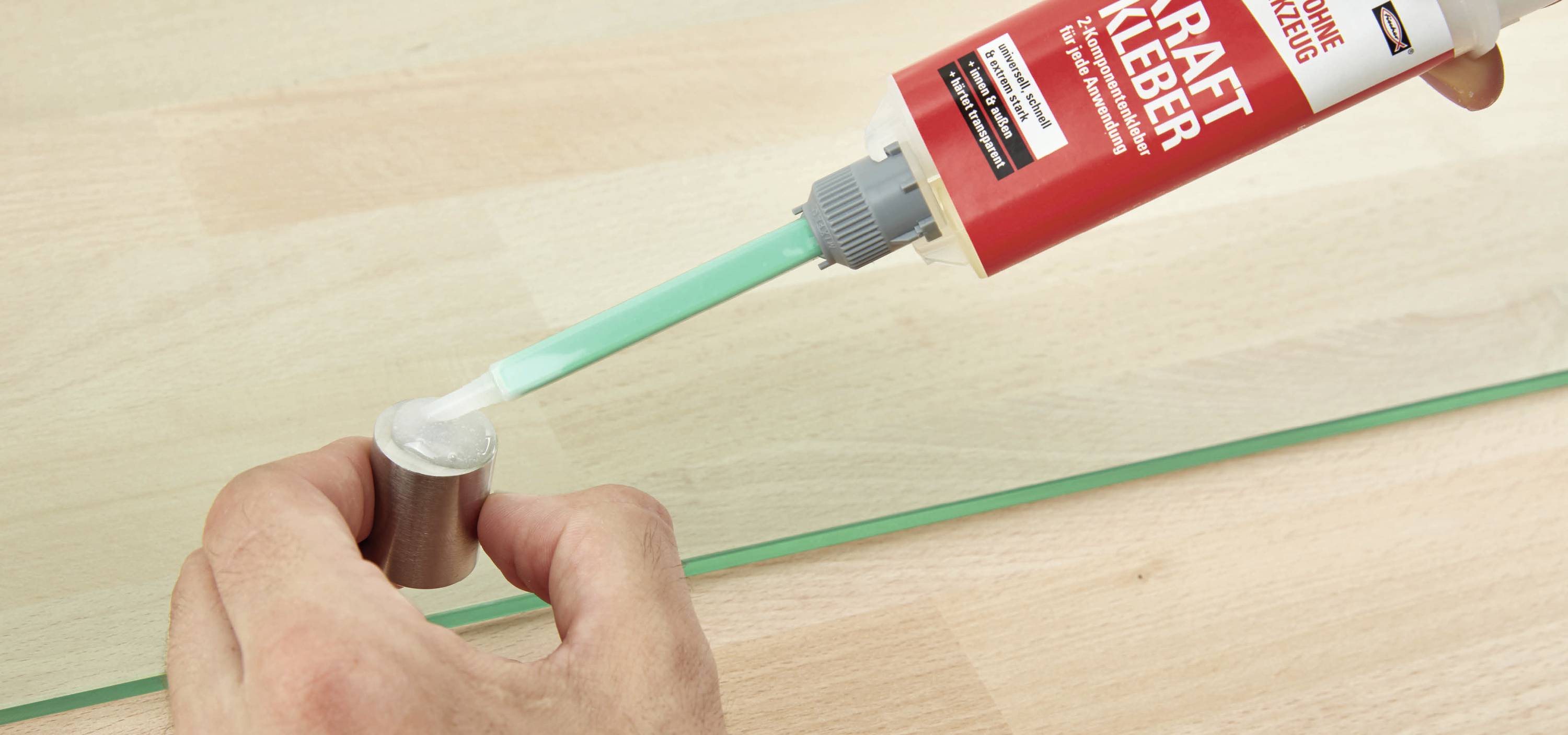 Eine Person trägt mit einer Spritze Kleber auf einen Metallzylinder auf, vermutlich zum Basteln oder Reparieren.