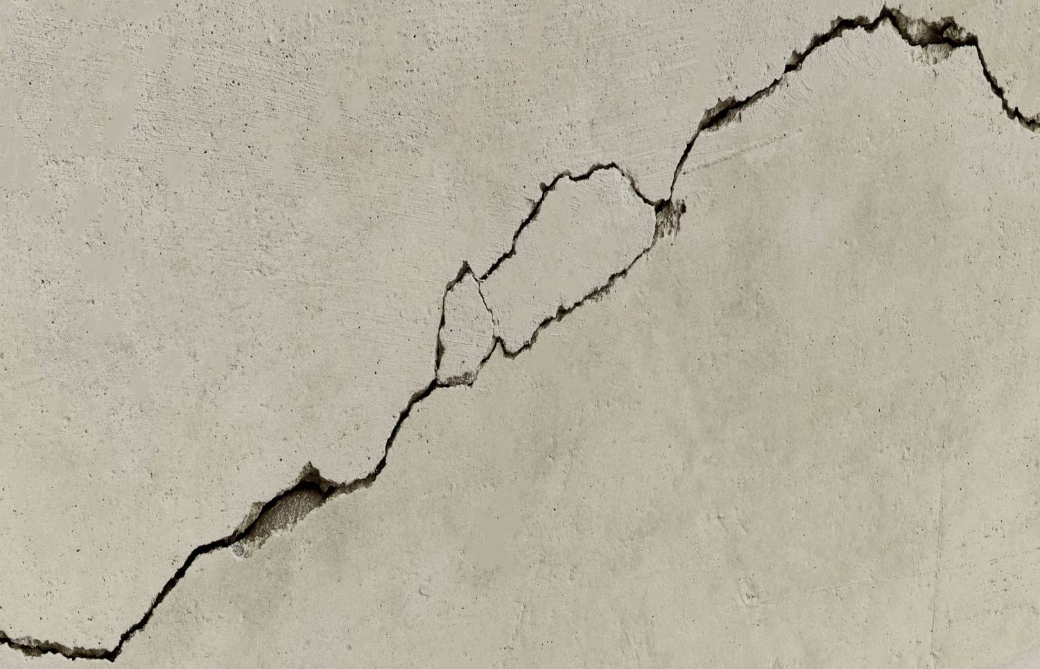 Riss in einer beige gestrichenen Betonwand, der diagonal verläuft.