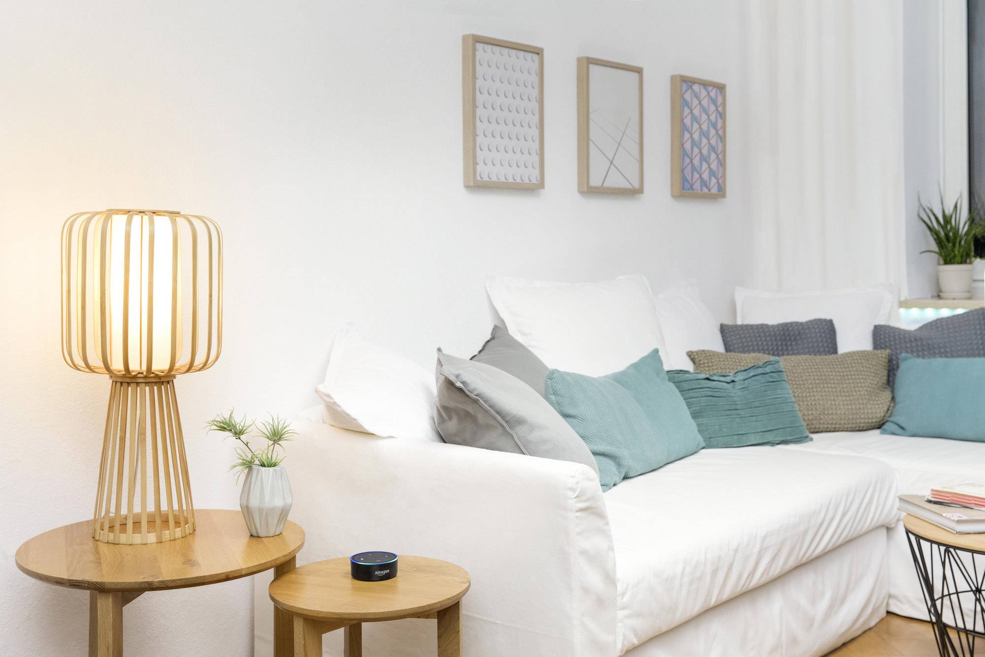 Wohnzimmer mit weißem Sofa, dekorativen Kissen und Holztisch. Eine Lampe leuchtet warm. An der Wand hängen moderne Bilder.