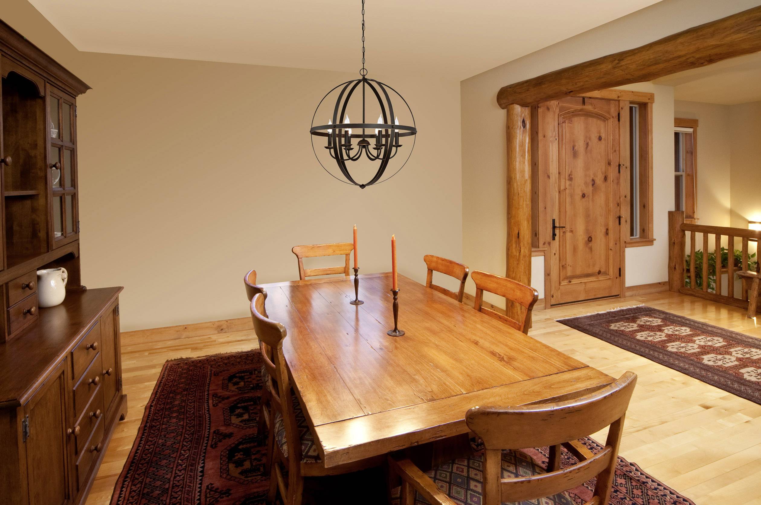 Esszimmer mit Holztisch, vier Stühlen und Retro-Kronleuchter. Holzböden und Schrank, Kerzenständer auf Tisch, rustikales Ambiente.
