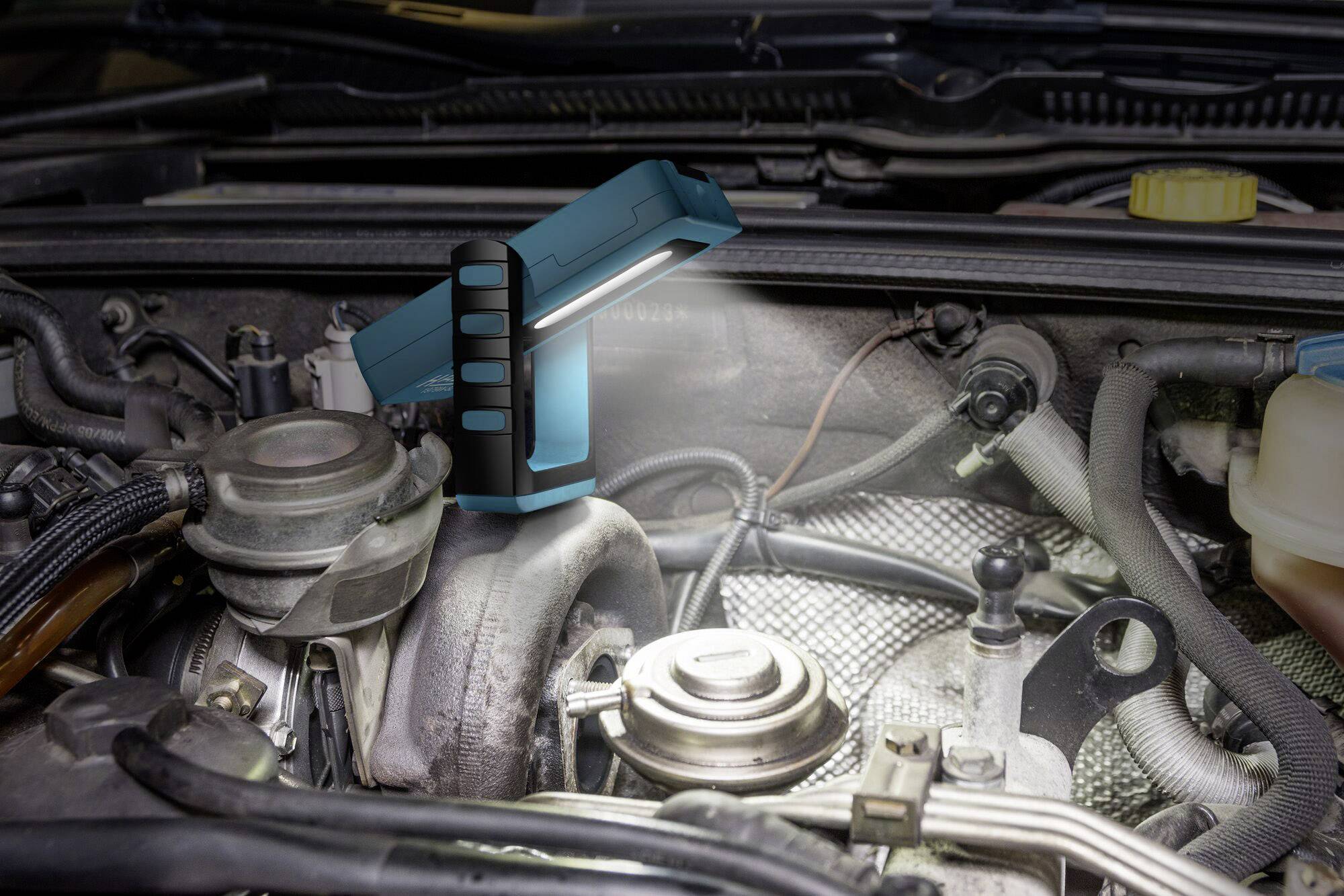Eine tragbare Lampe leuchtet den Motorraum eines Autos aus und ermöglicht eine klare Sicht auf den Turbo und umliegende Komponenten.