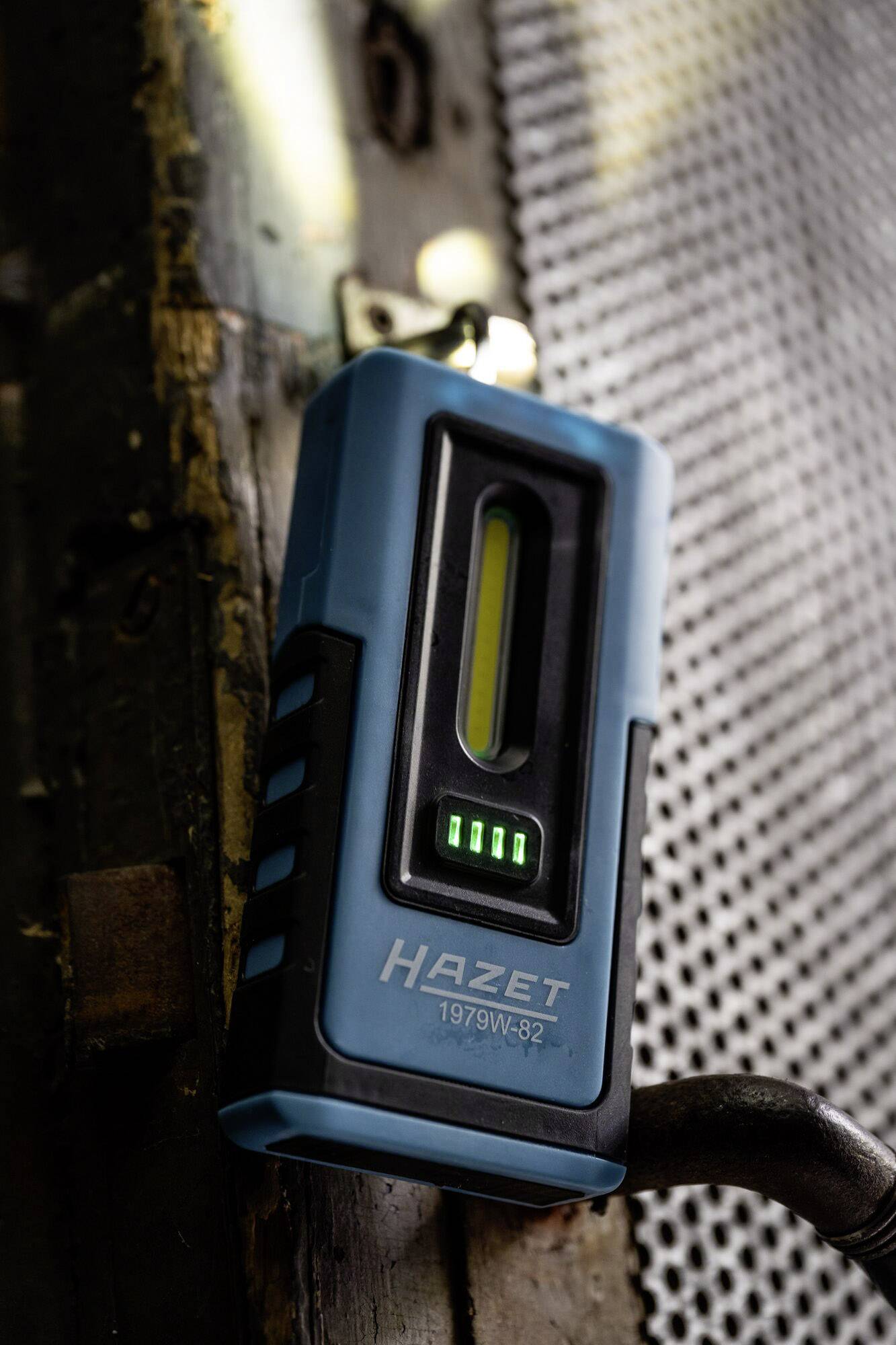 Tragbare blaue LED-Arbeitsleuchte mit HAZET-Logo, angeheftet an eine Metalloberfläche, zeigt vier grüne Ladeanzeigen.