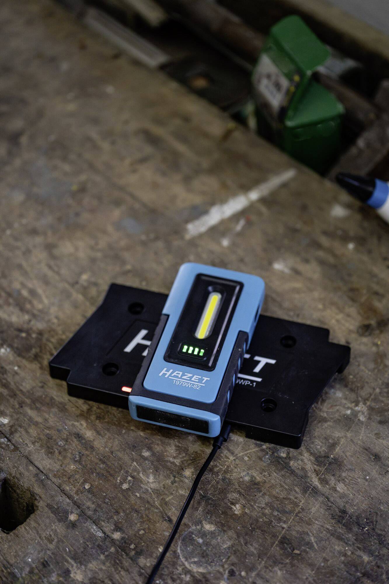 Ein blaues elektronisches Messgerät liegt auf einer schwarzen Halterung auf einem Holztisch. Es zeigt eine Leuchtanzeige.