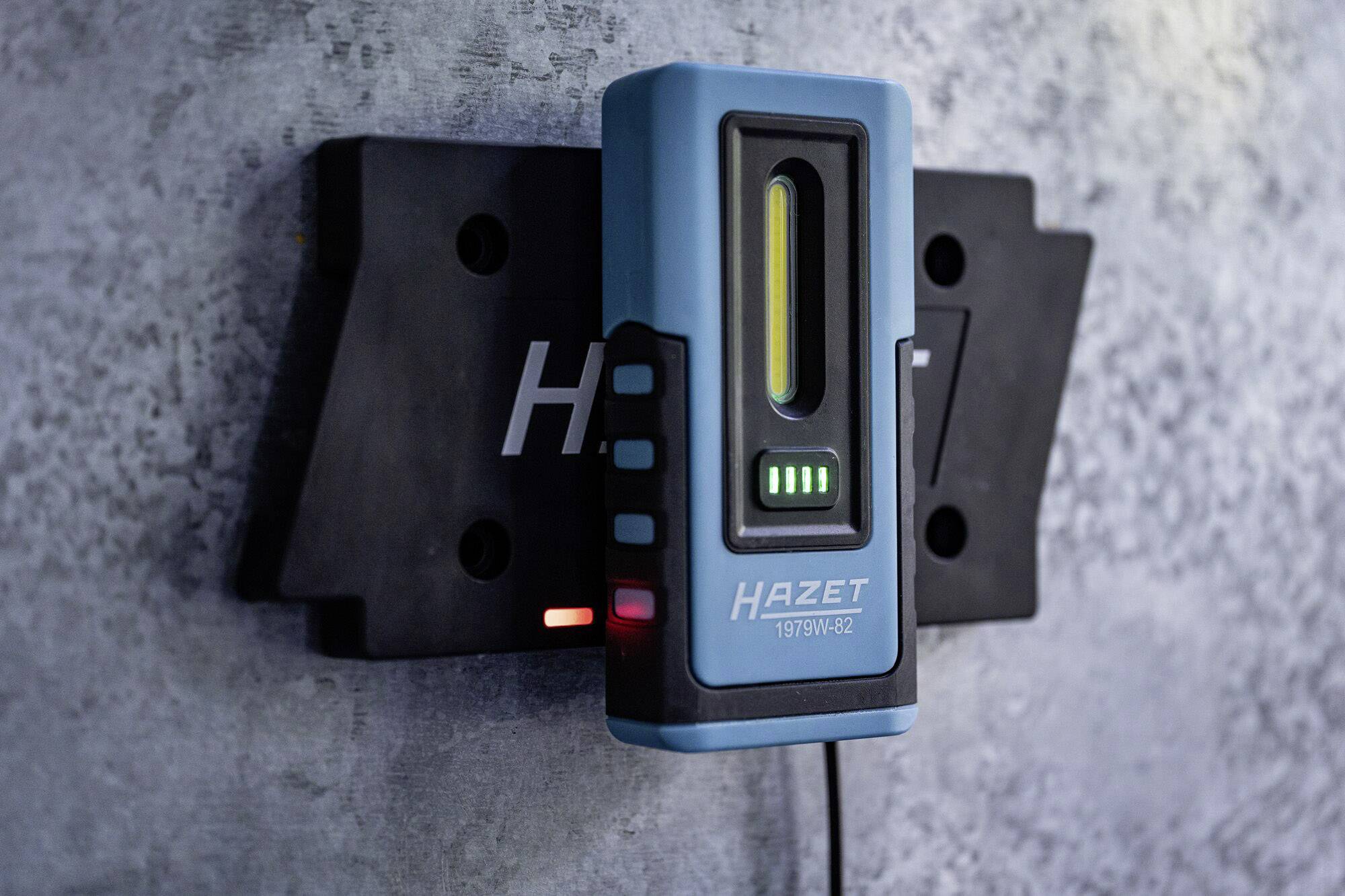 Ein blaues elektronisches Gerät zum Aufladen, montiert an einer Wandhalterung. Gerät zeigt Ladezustand mit grünen LEDs an.