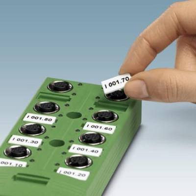 Hand wechselt Beschriftungsschild an einem grünen, elektronischen Gerät mit runden Steckplätzen, nummeriert von '001.10' bis '001.70'.
