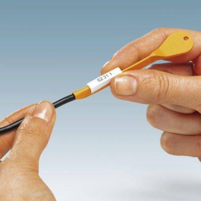 Eine Hand hält ein Kabel mit einer weißen Etikette, auf der 'S.211' steht. Die Szene zeigt die Vorbereitung oder Identifikation eines Kabels.