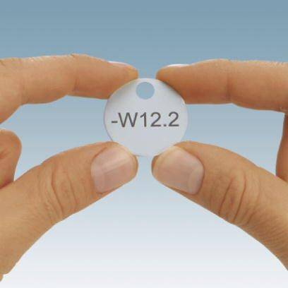 Zwei Hände halten eine kleine, durchsichtige Scheibe mit der Aufschrift '-W12.2' vor einem blauen Hintergrund.
