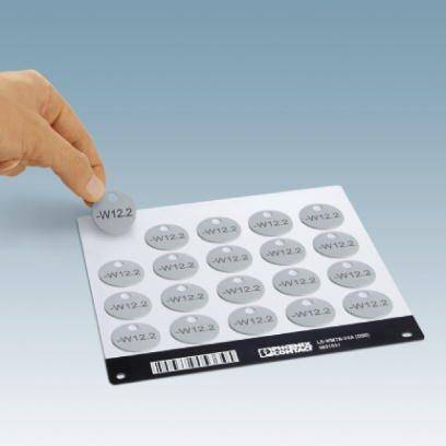 Eine Hand hebt einen runden Aufkleber mit der Aufschrift '-W12.2' von einer weißen Tafel mit mehreren identischen Aufklebern ab.