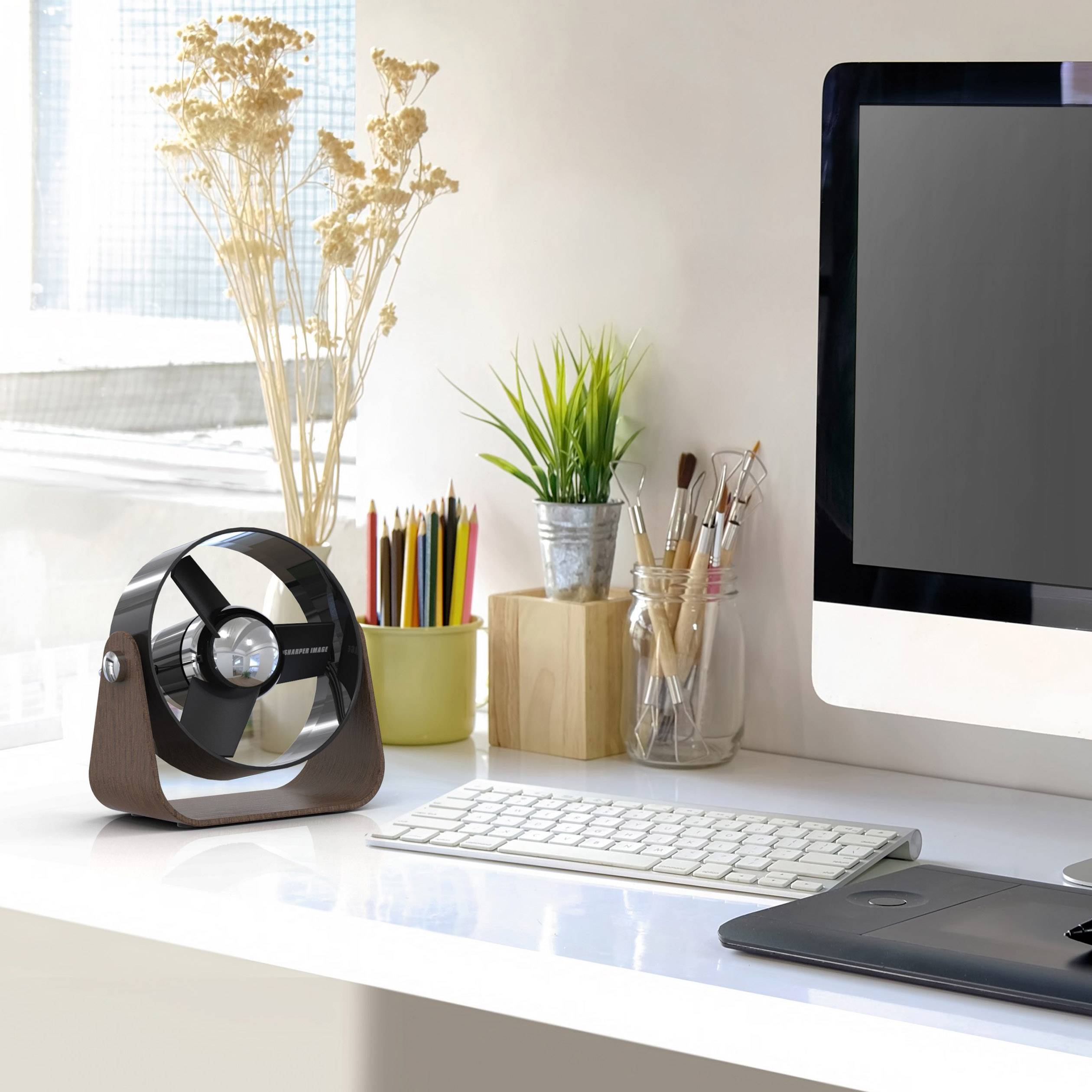 Moderner Arbeitsplatz mit Computer, Tastatur, Maus und Stift-Tablet. Pflanzen und ein kleiner Ventilator stehen auf dem Schreibtisch.
