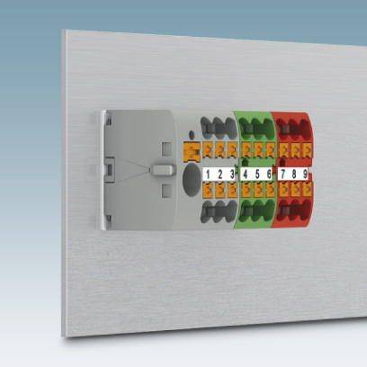Ein elektrischer Verbinder mit nummerierten Klemmen von 1 bis 9, in drei Farben: Schwarz, Grün und Rot, auf einer grauen Platte montiert.