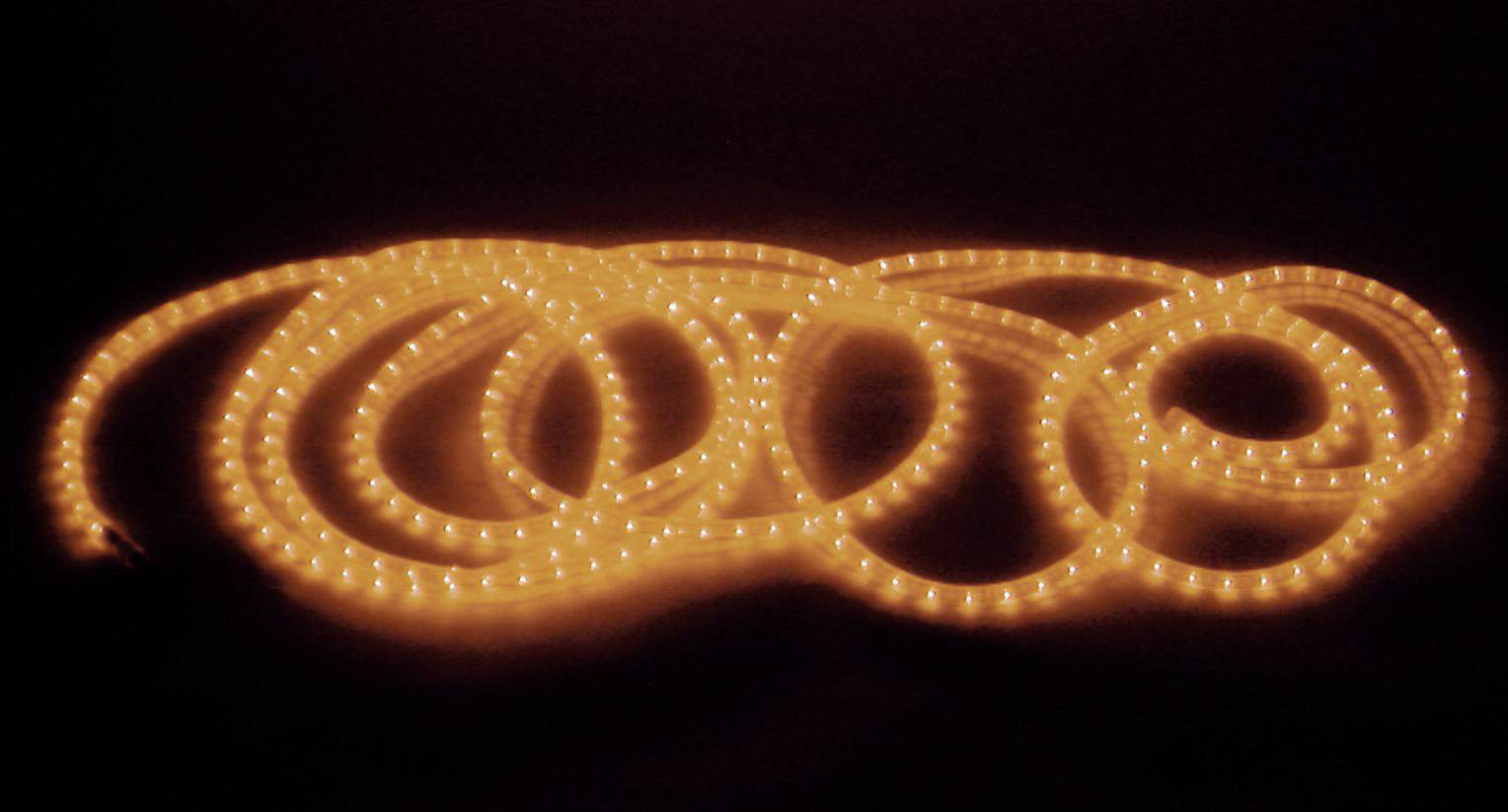 Ein leuchtender LED-Lichtschlauch in einer dunklen Umgebung, gewunden in mehreren Schleifen auf dem Boden liegend.