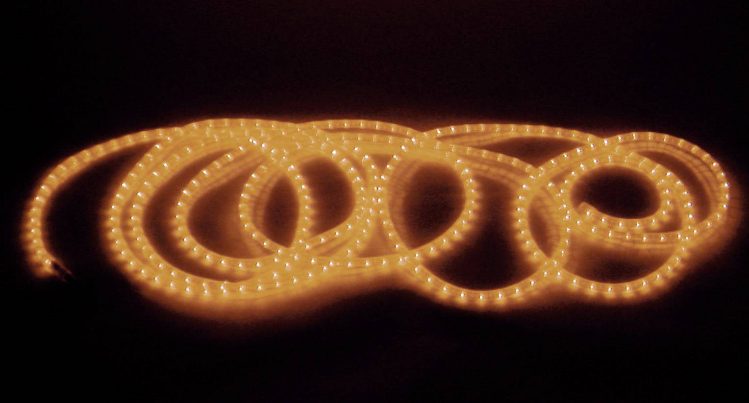 Ein leuchtender LED-Lichtschlauch in einer dunklen Umgebung, der in mehreren Schlaufen liegt und warmes, gelbes Licht ausstrahlt.