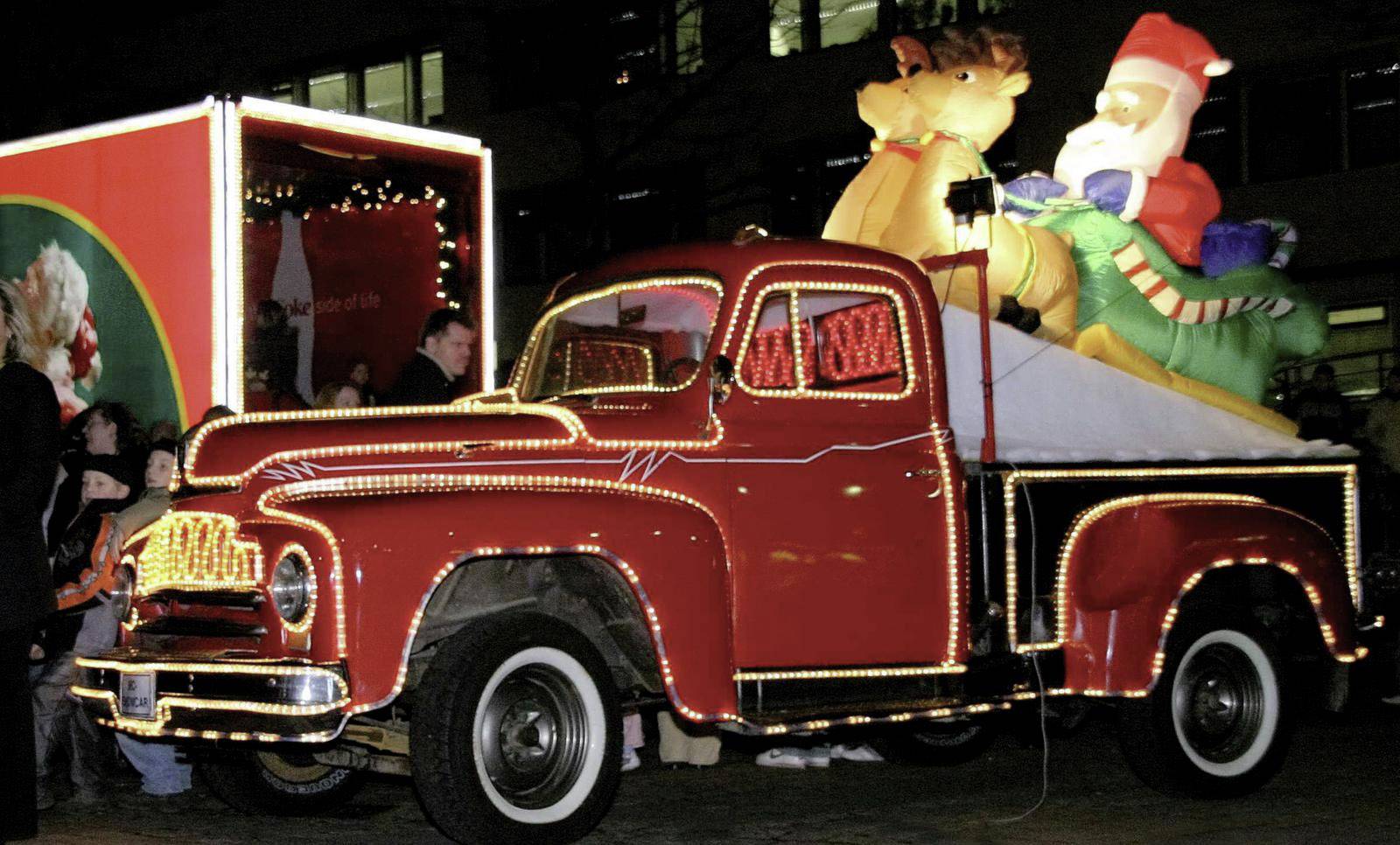 Ein roter, festlich beleuchteter Lastwagen mit einer Santa- und Rentier-Dekoration auf der Ladefläche bei Nacht.