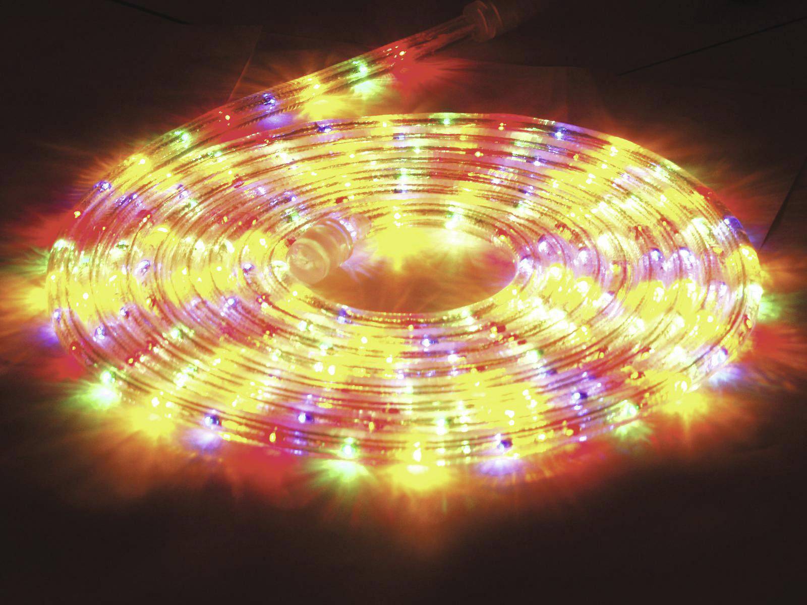 Ein leuchtender LED-Lichtschlauch in verschiedenen Farben, der in einer Spirale auf dem Boden liegt. Er strahlt hell in Rot, Gelb, Grün und Blau.