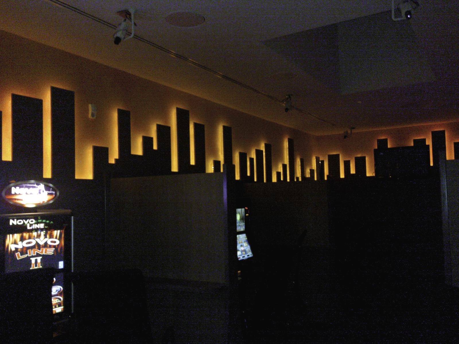 Eine dunkle Spielhalle mit beleuchteter Skyline-Dekoration an der Wand. Spielautomaten sind im schwachen Licht zu sehen.