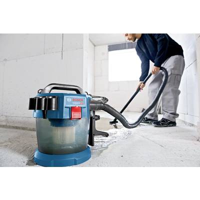 Ein Mann reinigt mit einem Bosch Bau-Staubsauger einen Betonboden in einem hellen Raum. Der Staubsauger ist blau und transparent.