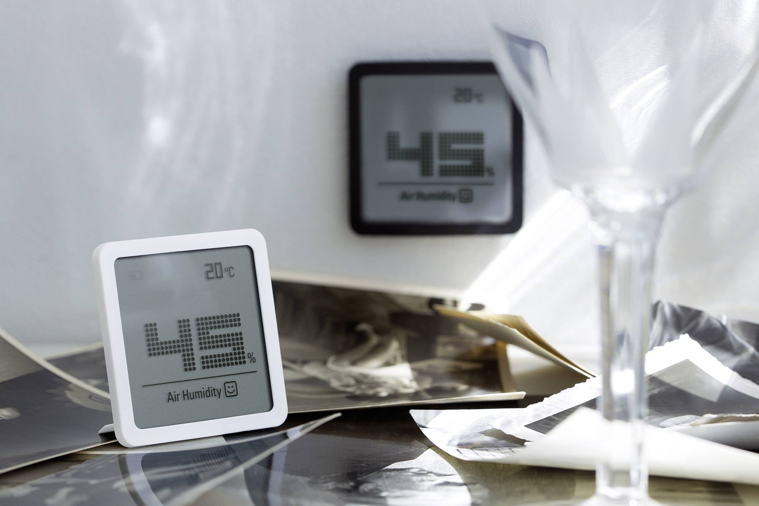 Mehrere Messgeräte mit digitalen Anzeigen in einem Raum. Im Vordergrund sind Fotos auf einem Tisch und ein Glas zu sehen.