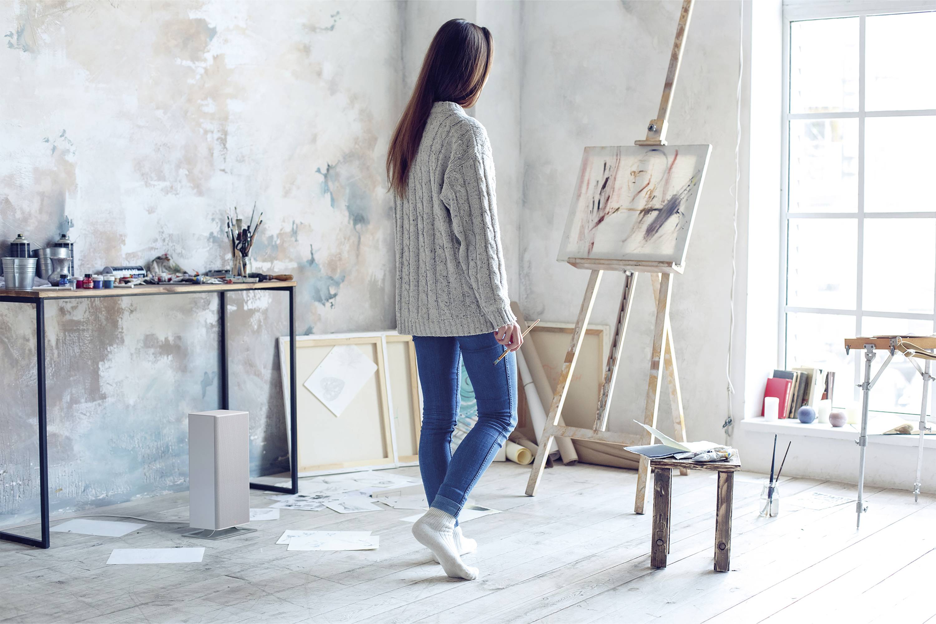 Ein Mensch betrachtet ein abstraktes Gemälde auf einer Staffelei in einem Atelier mit Kunstmaterialien und Zeichnungen im Hintergrund.