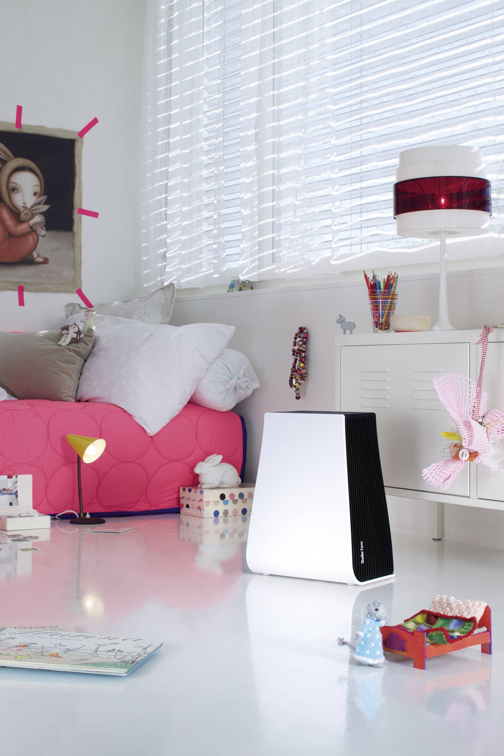 Ein helles, modernes Wohnzimmer mit rosa Sofa und Dekorationen; im Vordergrund steht ein stilvolles Luftreinigergerät auf weißem Boden.