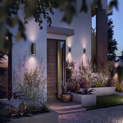 Moderne Außenansicht eines Hauses mit beleuchteten Pflanzen und stilvoller Wandbeleuchtung. Abenddämmerung schafft stimmungsvolle Atmosphäre.