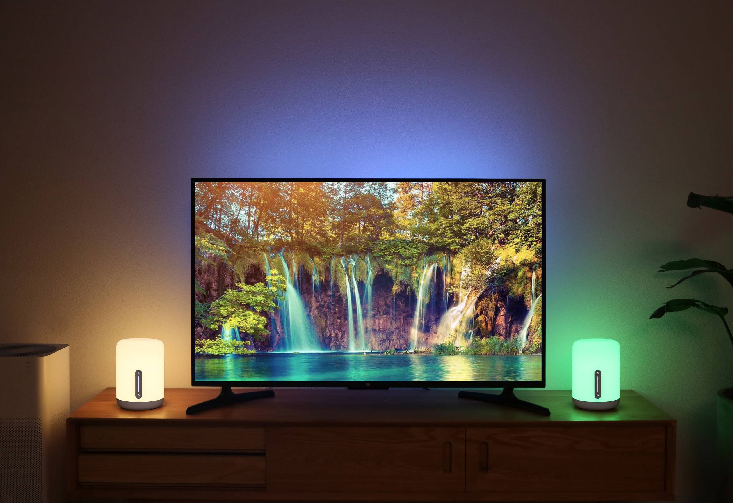 Ein Fernseher zeigt ein Landschaftsbild von Wasserfällen. Daneben stehen zwei Lampen, die in Blau und Grün leuchten und die Umgebung erhellen.