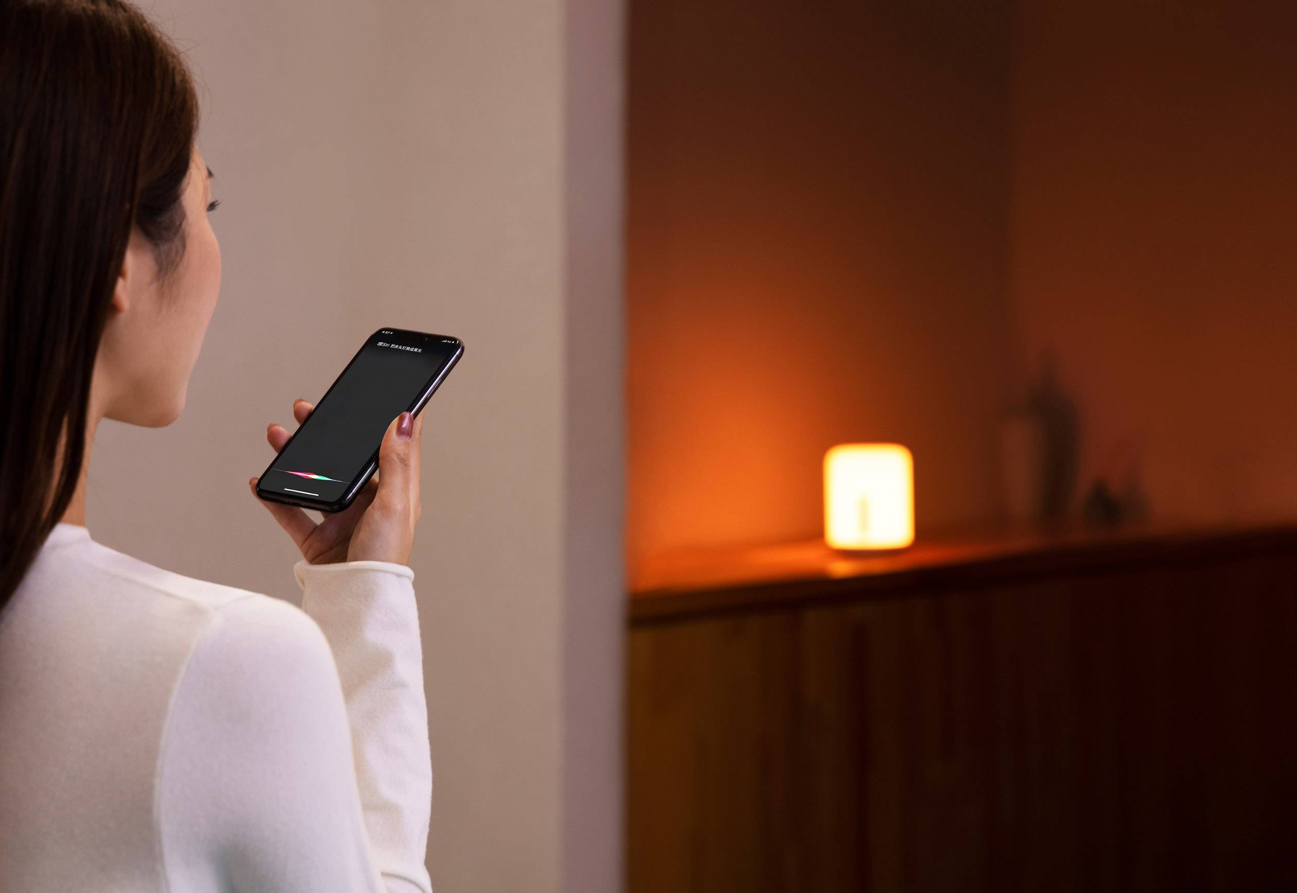 Eine Person nutzt eine Sprachassistent-Funktion auf einem Smartphone, während im Hintergrund eine orangefarbene Lampe leuchtet.