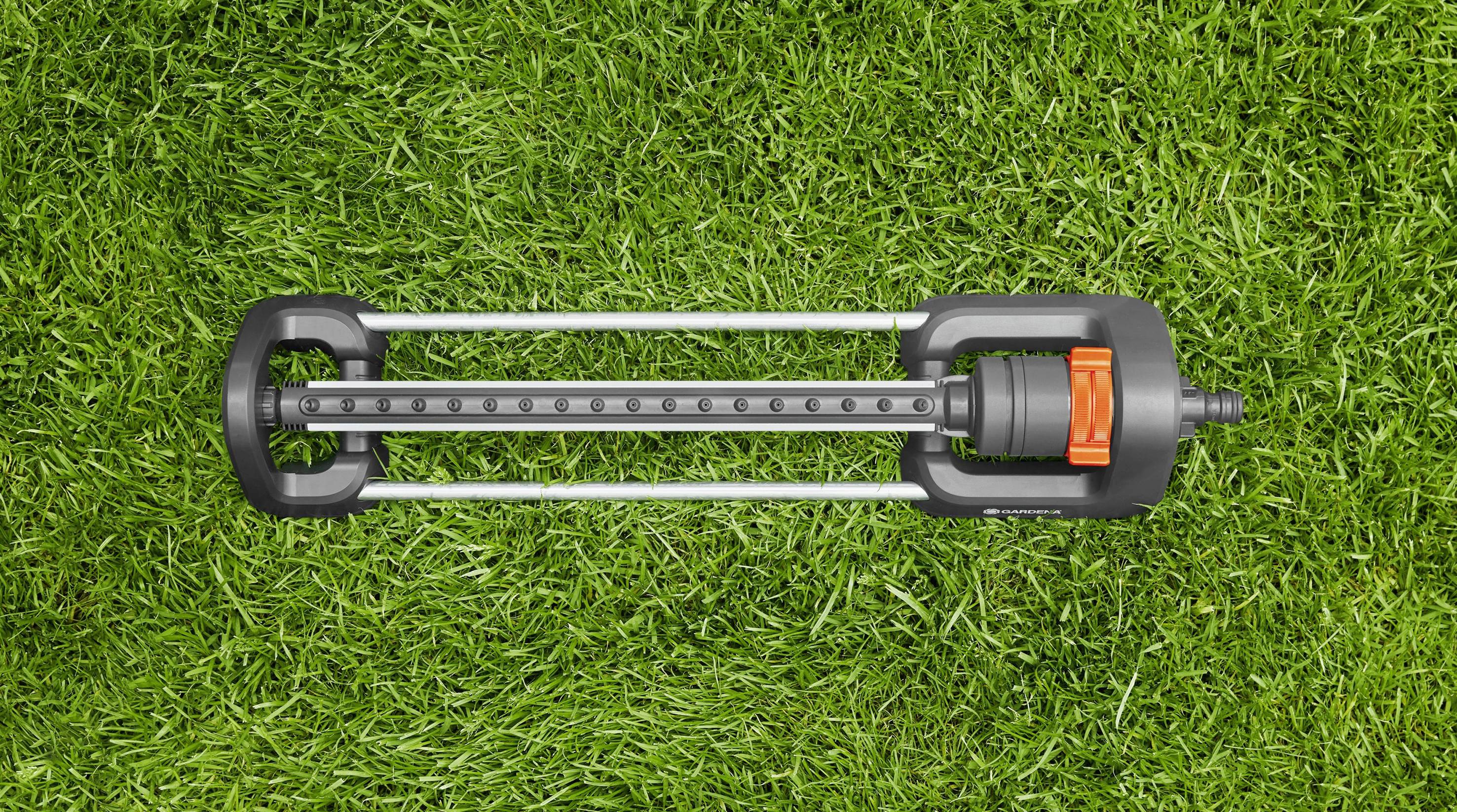 Ein Rasensprenger liegt auf grünem Gras. Es handelt sich um einen oszillierenden Sprinkler mit schwarzem und orangem Design.