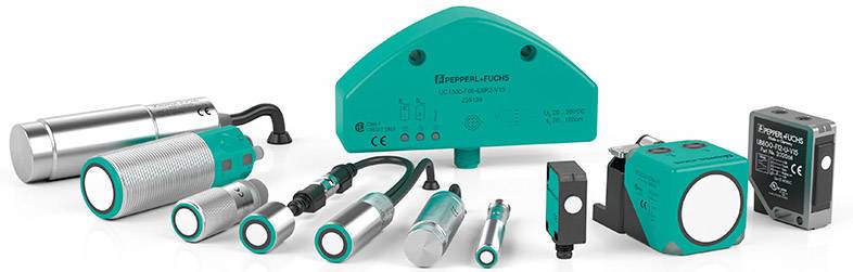 Verschiedene Sensoren von Pepperl+Fuchs in einer Linie angeordnet, darunter zylindrische und rechteckige Modelle in silberner und grüner Farbe.
