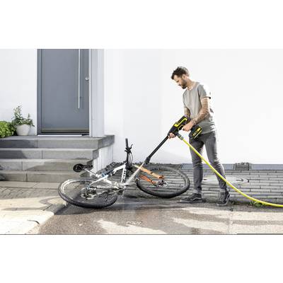 Ein Mann reinigt ein Fahrrad mit einem Hochdruckreiniger vor einem Hauseingang.