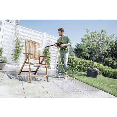 Ein Mann reinigt mit einem Hochdruckreiniger einen Holzstuhl auf einer Terrasse im Garten an einem sonnigen Tag.