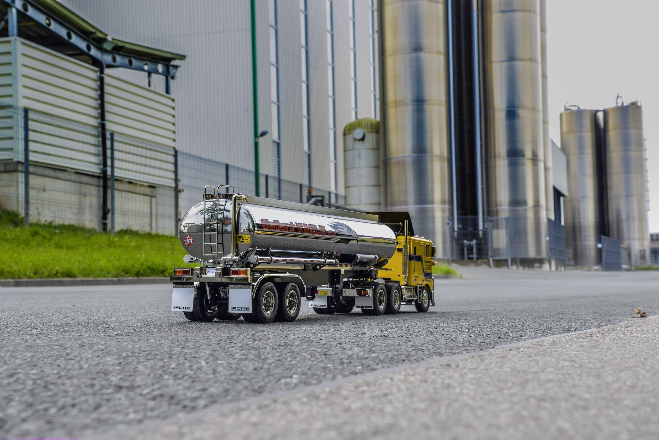 Ein Miniaturtanklastwagen fährt eine leere Straße entlang. Im Hintergrund sind hohe Industriegebäude zu sehen.