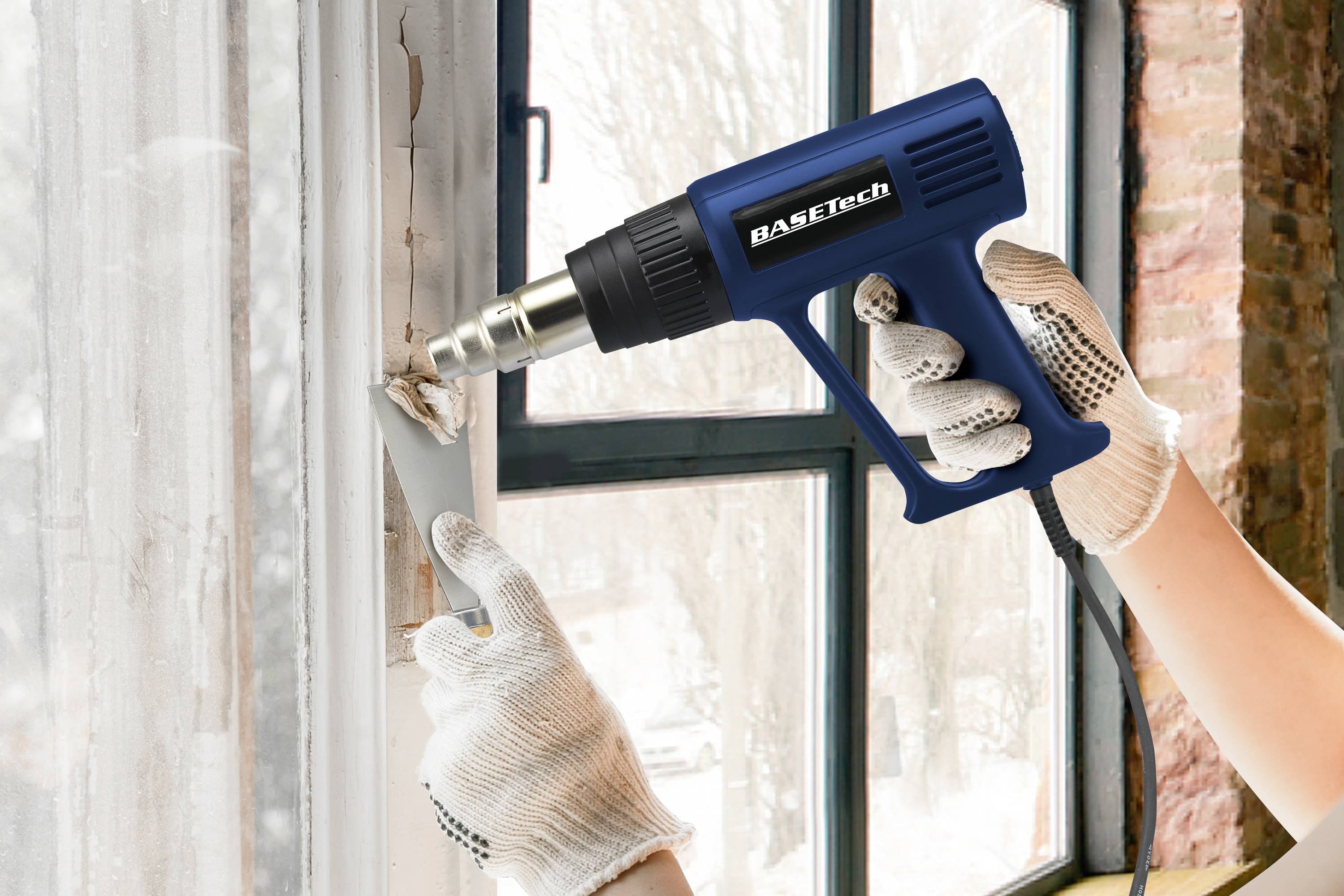 'Person entfernt Farbe von einem Fensterrahmen mit einem blauen Heißluftfön und einem Spachtel, Hände tragen weiße Handschuhe.'