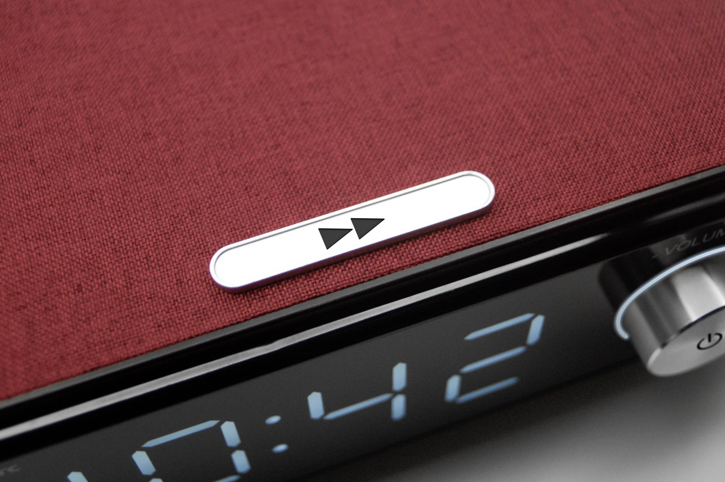 Ein digitaler Wecker mit rotem Stoffbezug zeigt die Zeit 10:42 an. Ein Knopf für Wiedergabe und Pause ist deutlich sichtbar.