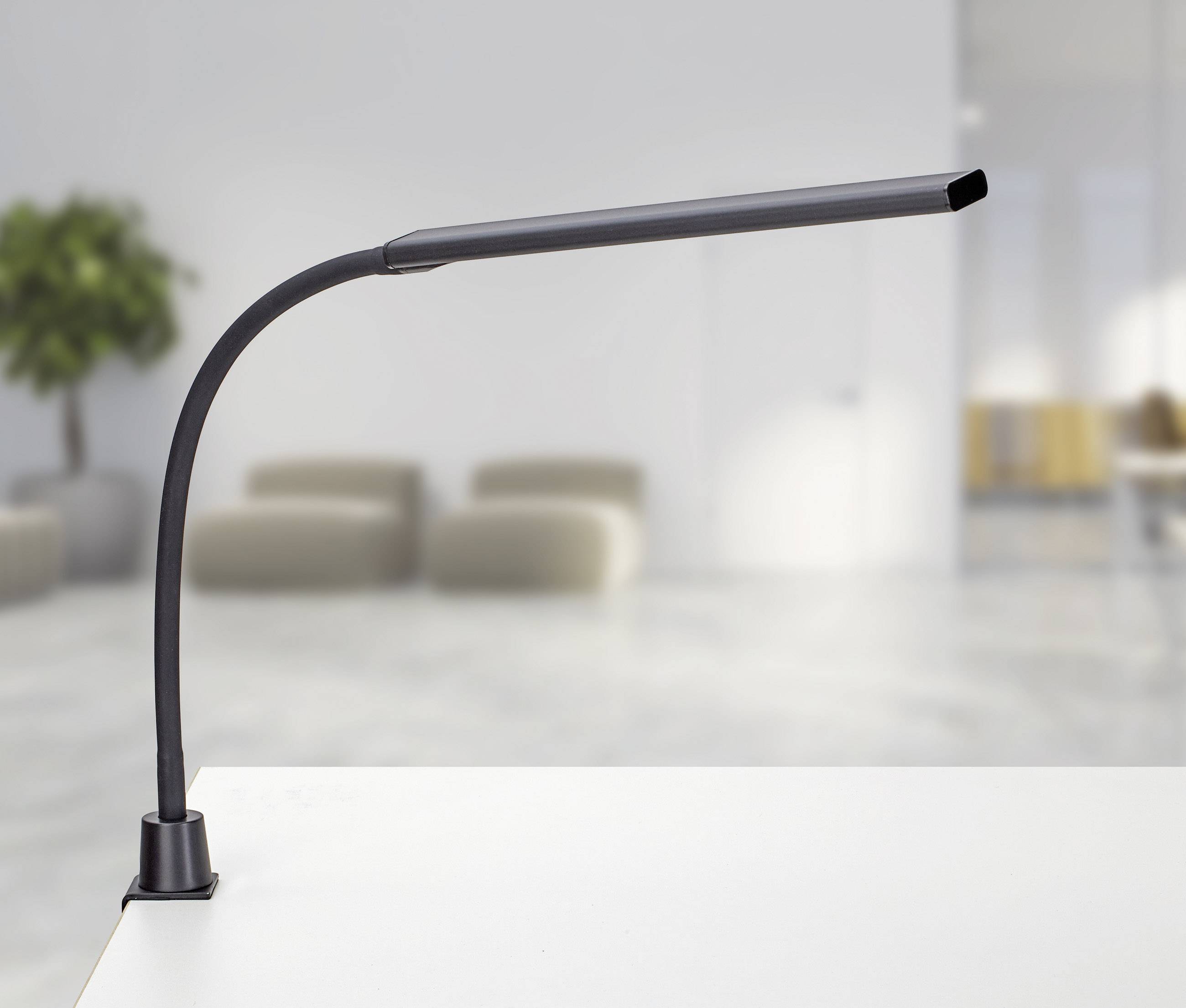 Schwarze, flexible LED-Schreibtischlampe auf einem weißen Tisch in modernem, minimalistischem Raum mit verschwommenem Hintergrund.