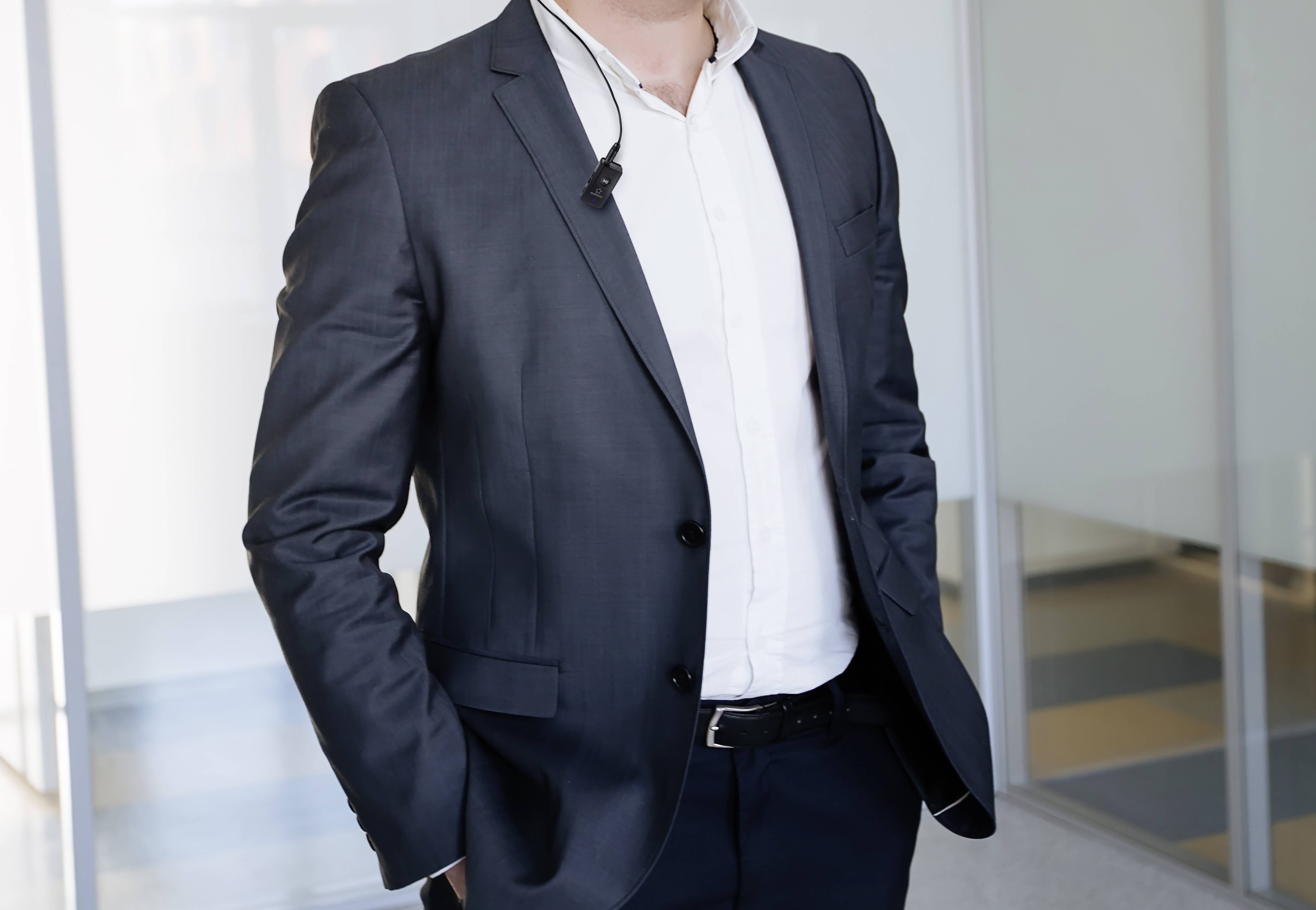 Geschäftsmann in Anzug steht in modernem Büro, telefoniert mit einem Ohrhörer.