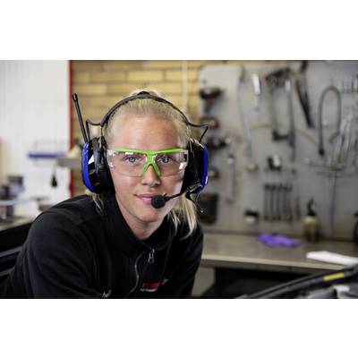 Eine Frau in Schutzbrille und Kopfhörer mit Mikrofon in einer Werkstattumgebung. Im Hintergrund sind Werkzeuge sichtbar.