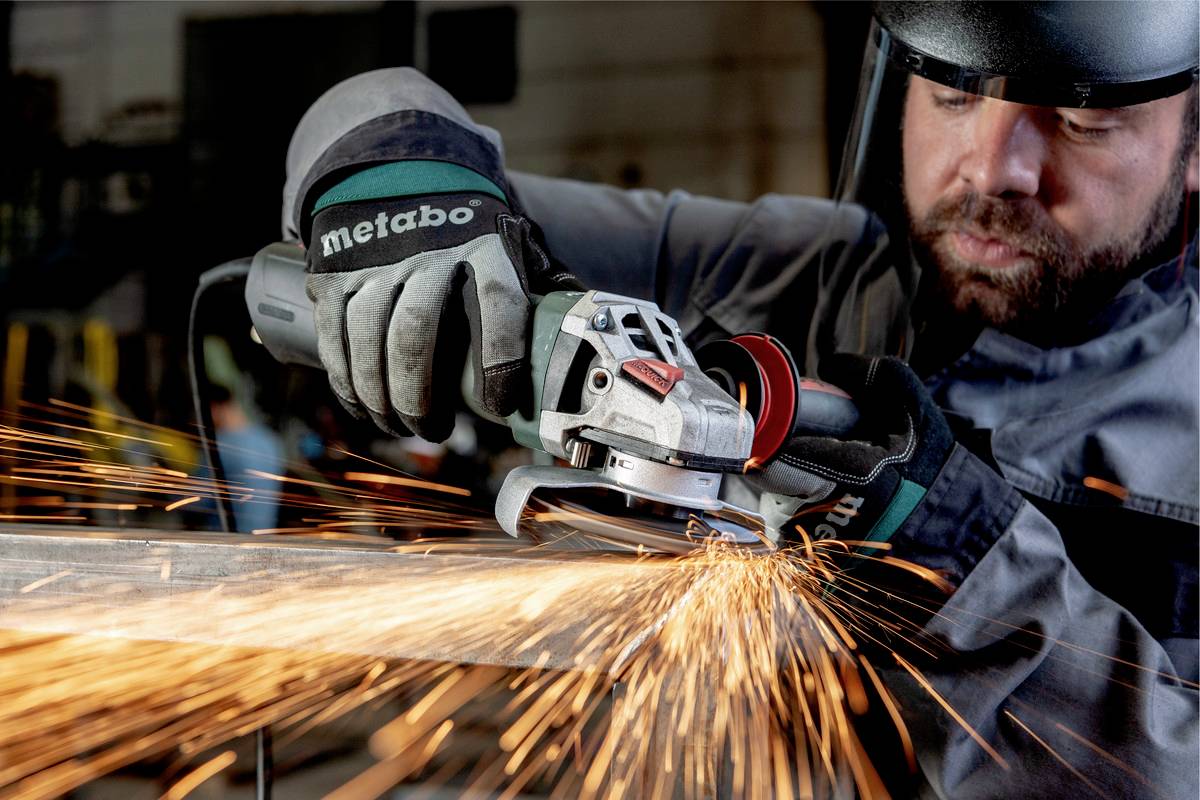 Eine Person in Schutzkleidung schleift mit einem Winkelschleifer Metall, Funken fliegen.