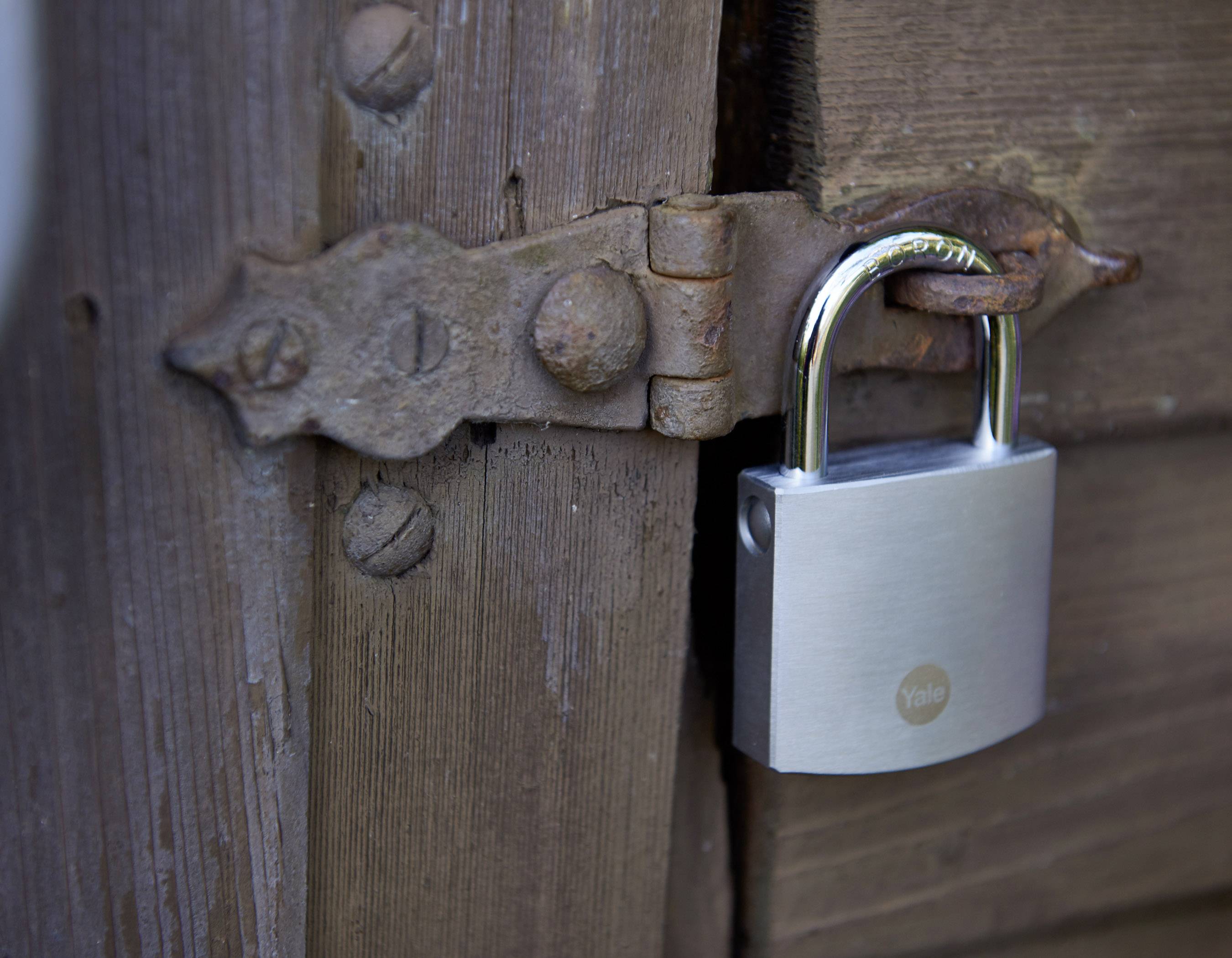 Ein silbernes Vorhängeschloss sichert eine Holztür mit rostigem Scharnier.