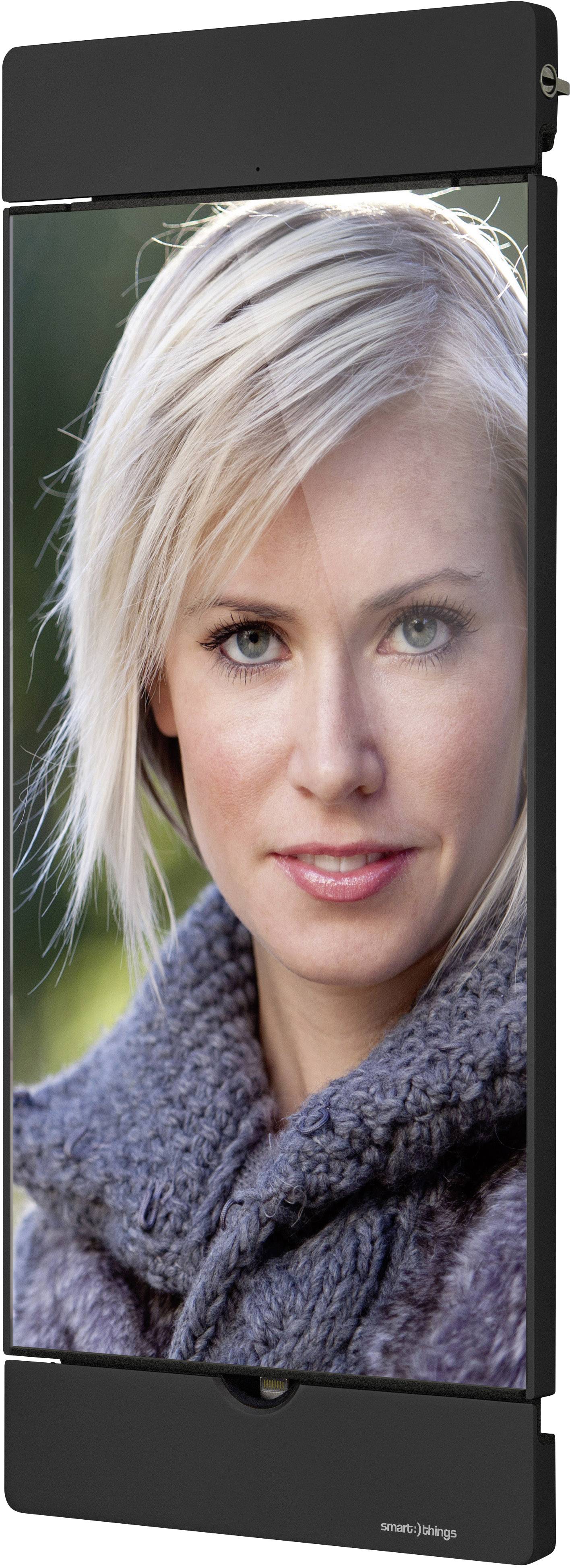 Eine Frau mit blonden Haaren und einem grauen Schal lächelt leicht, während sie direkt in die Kamera schaut. Hintergrund ist unscharf.