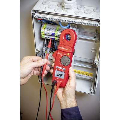 Eine Person hält ein Digitalmultimeter vor einem geöffneten Sicherungskasten und misst eine Spannung von 404,6 Volt.